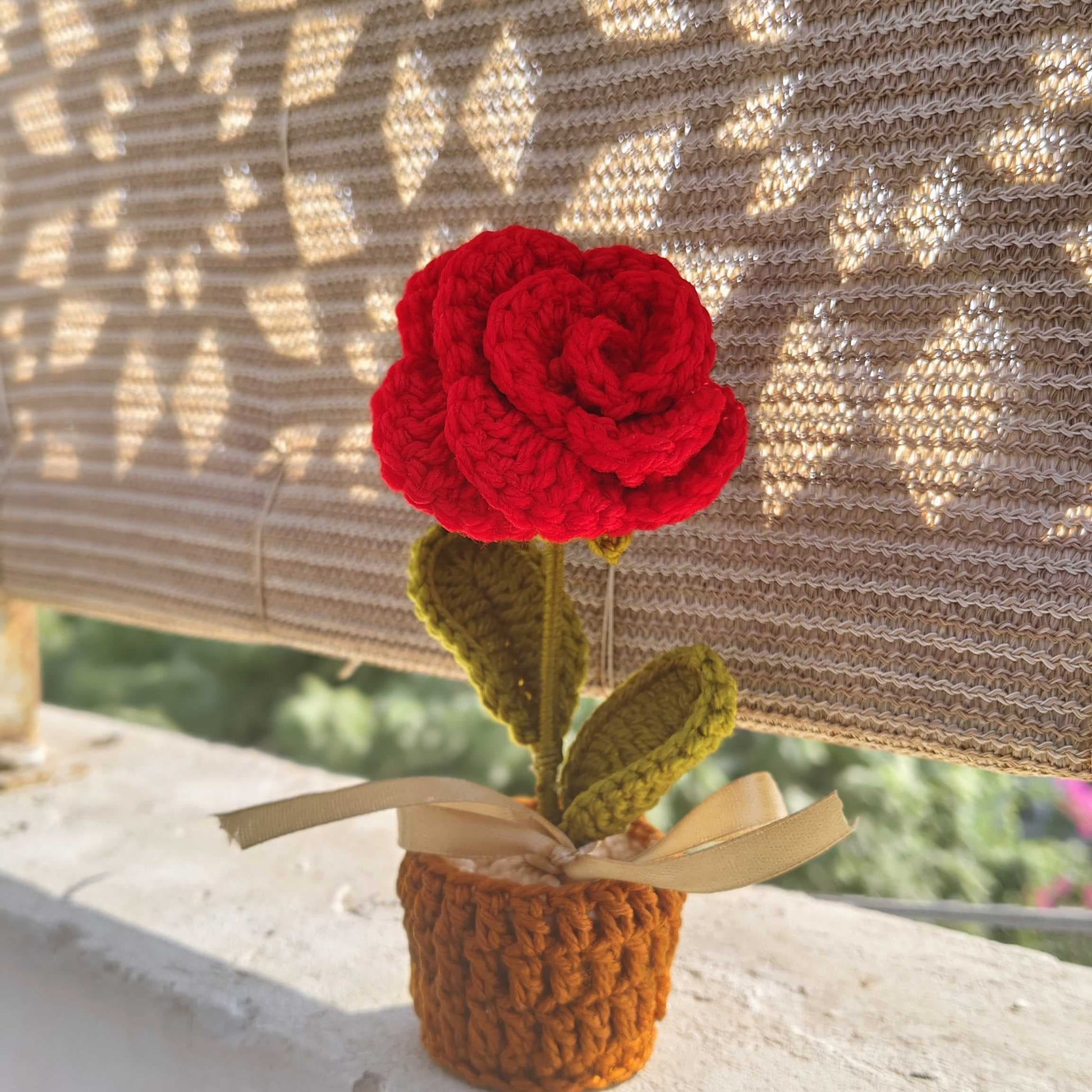 Crocheted red rose in a small pot against a textured wall.