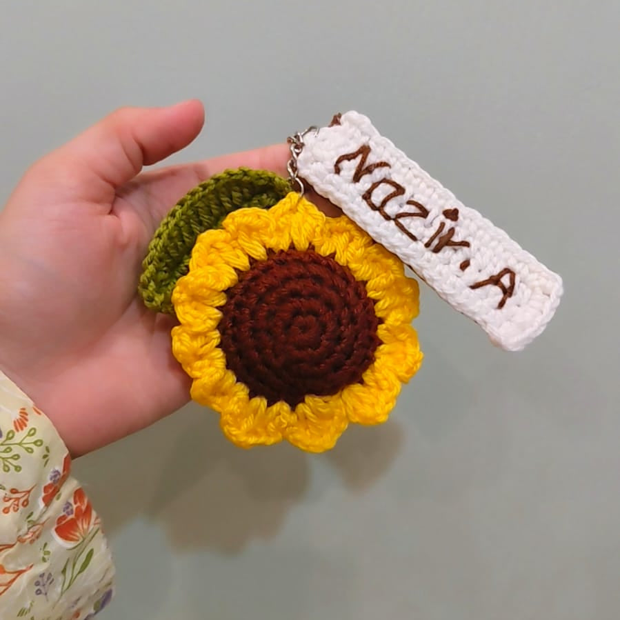 Hand holding a sunflower-shaped keychain with a name tag on a plain background