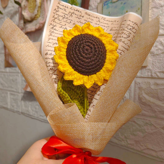 Handmade sunflower decoration in a burlap wrap with a red ribbon, held against a textured wall.
