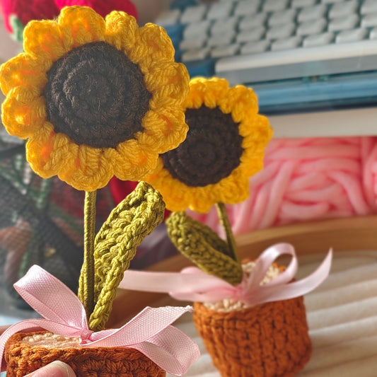 Handmade crochet sunflowers with ribbons on a textured surface.