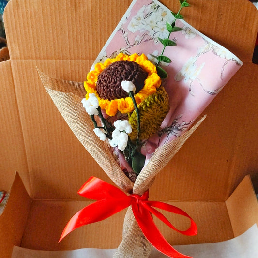 Bouquet of knitted flowers with a red ribbon on a cardboard box background