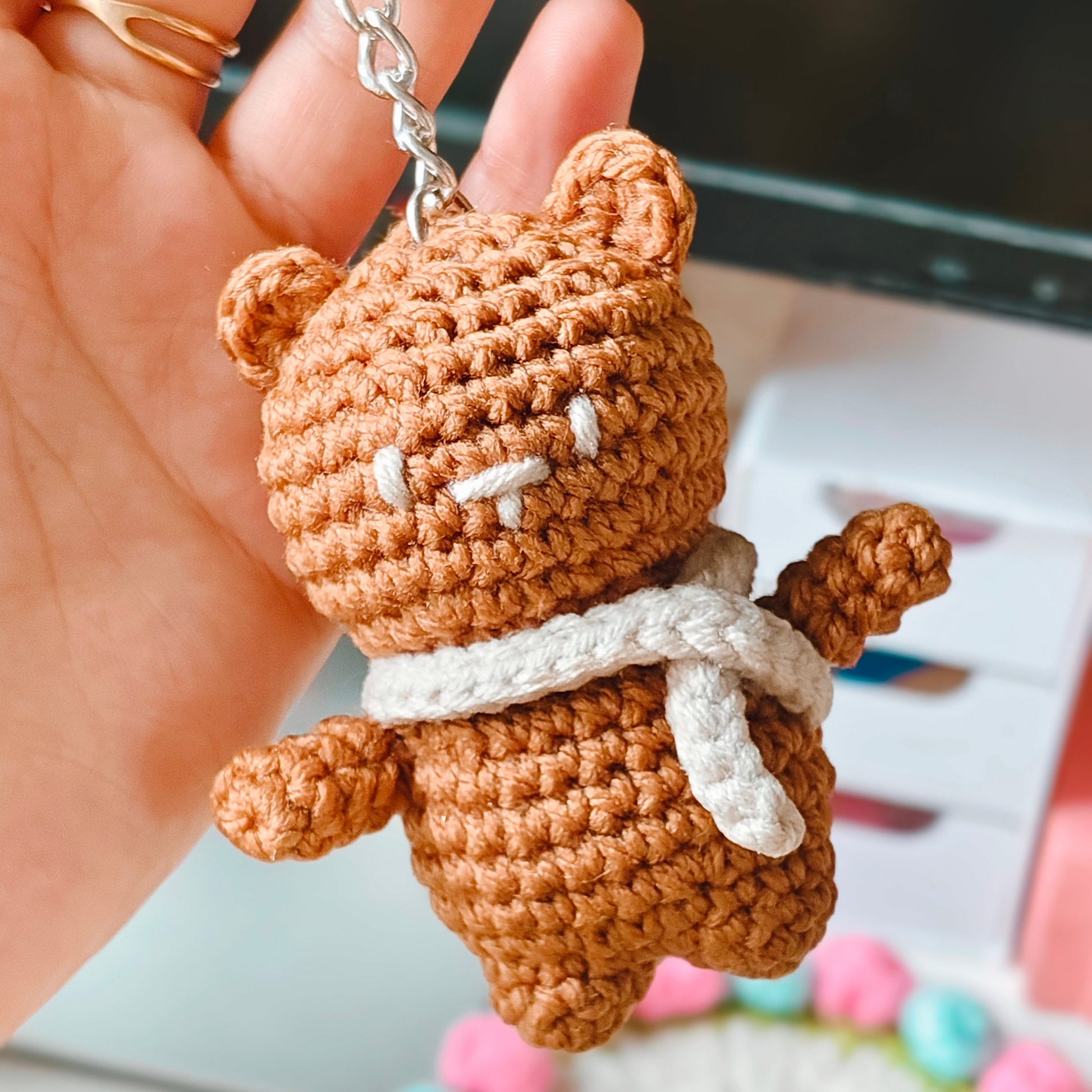 Brown teddy bear keychain held by a hand with a blurred background