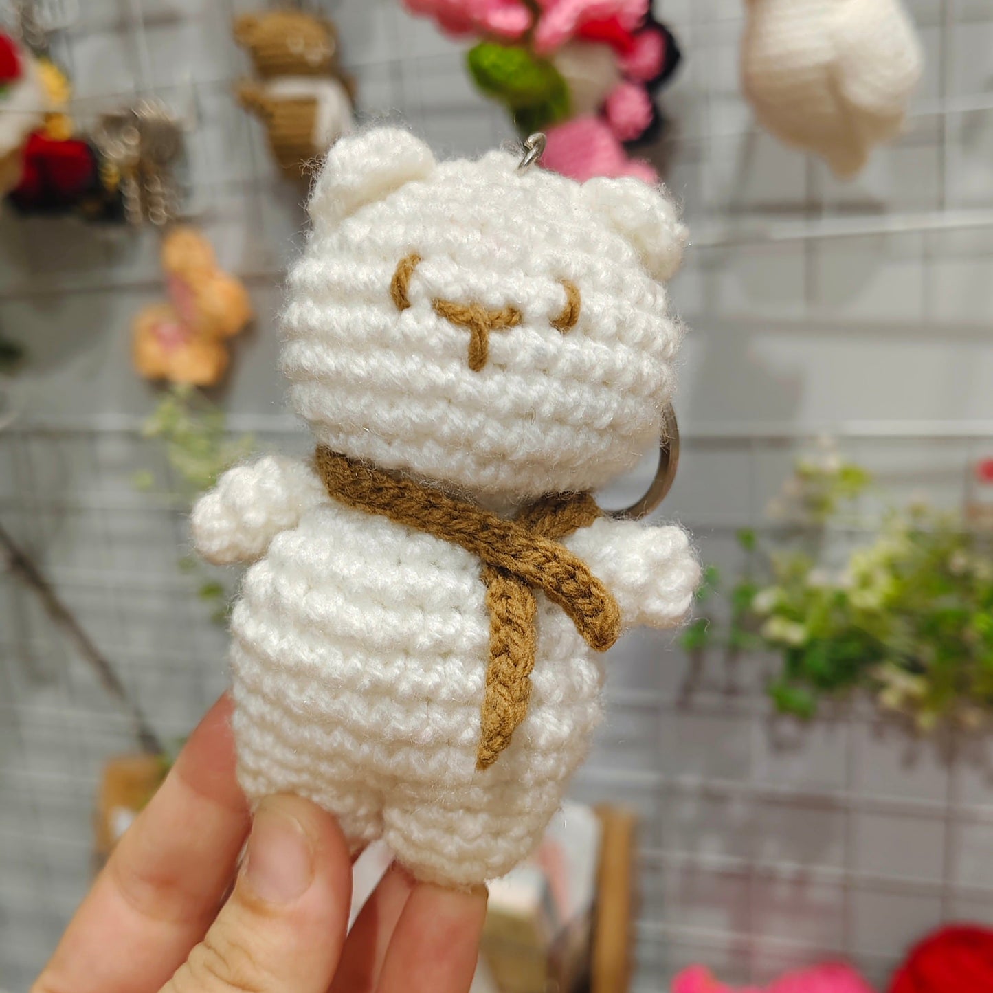 Handmade crochet bear keychain held in front of a display of various colorful keychains.