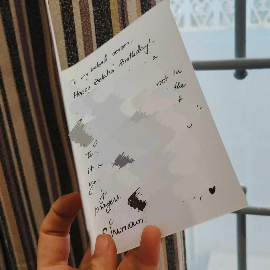 Hand holding a card with text and black illustrations against a striped curtain background