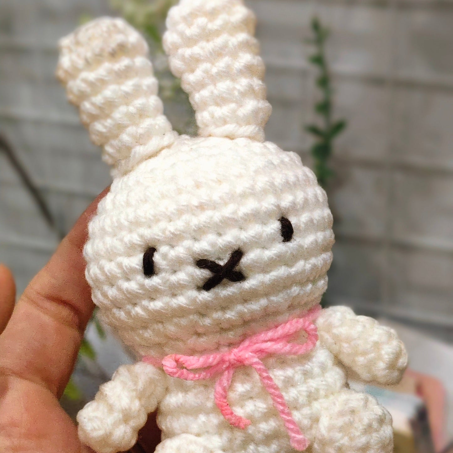 White crocheted bunny with a pink bow held in a hand against a blurred background
