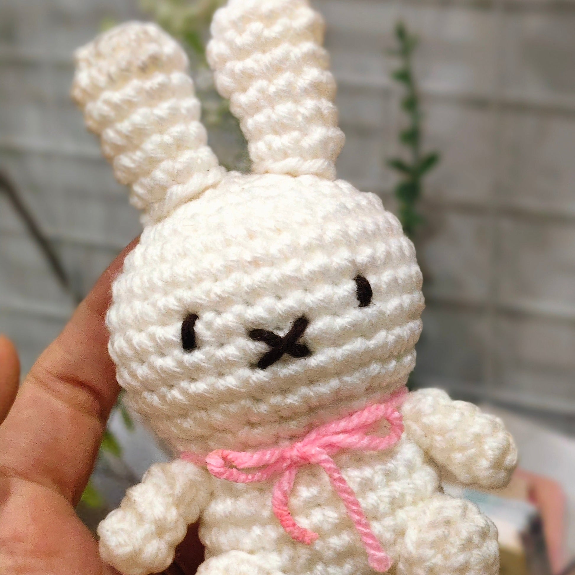 White crocheted bunny with a pink bow held in a hand against a blurred background