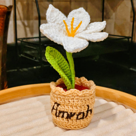 Knitted white flower with green stem in a woven pot on a textured surface