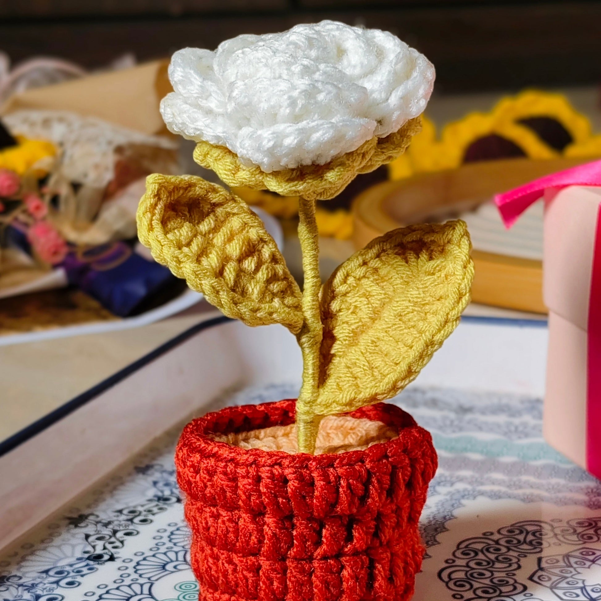 Crocheted white rose in a pot on a patterned surface