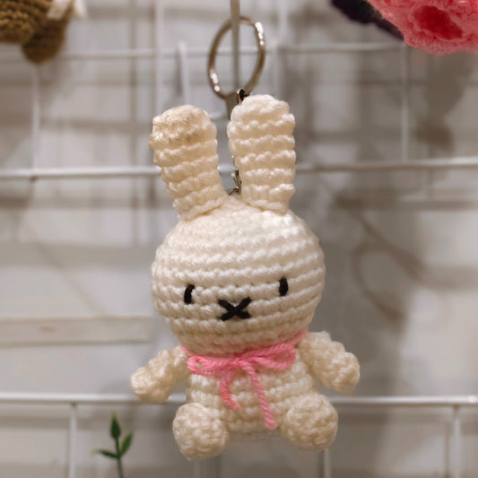 Crocheted bunny keychain with a pink bow on a wire rack.